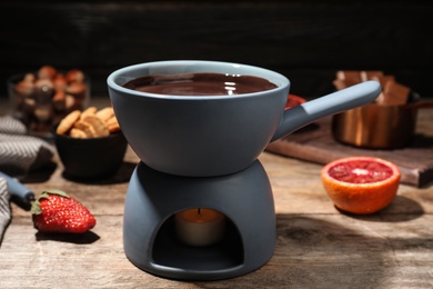 Photo of Ceramic pot with chocolate fondue on wooden table