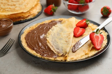Photo of Delicious thin pancakes with chocolate spread and raspberries on grey table, closeup