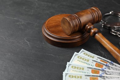 Photo of Judge's gavel, money and handcuffs on dark grey table, closeup. Space for text