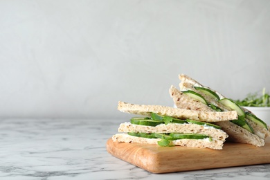 Photo of Wooden board with traditional English cucumber sandwiches on table. Space for text