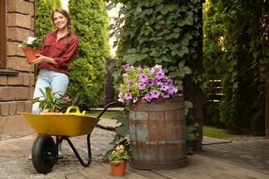 Photo of Female gardener with wheelbarrow and plants outdoors