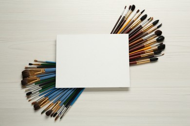 Photo of Blank canvas and brushes on white wooden table, flat lay. Space for text