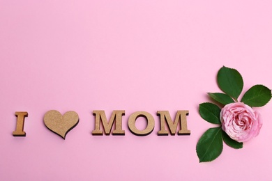 Photo of Phrase I LOVE MOM made of wooden letters with heart and flower for Mother's Day on color background