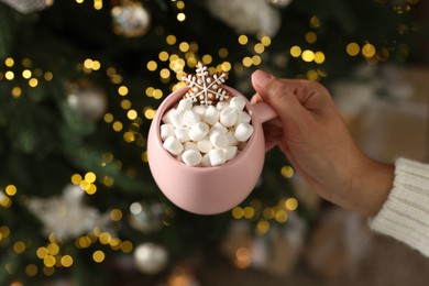 Photo of Woman holding cup of delicious Christmas cocoa with marshmallows and gingerbread against blurred lights, above view