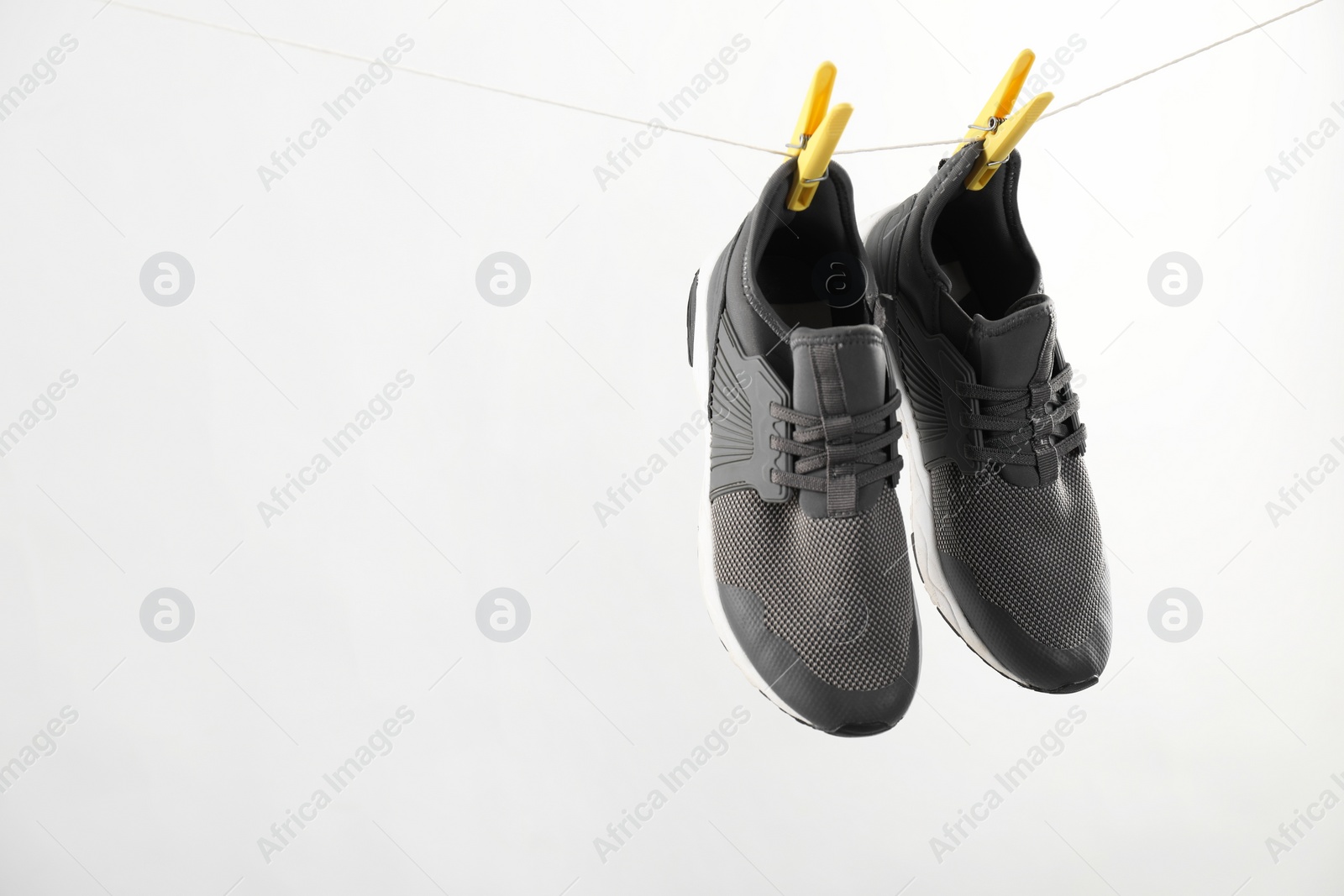 Photo of Stylish sneakers drying on washing line against light grey background, space for text