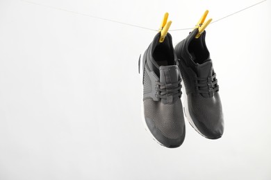 Stylish sneakers drying on washing line against light grey background, space for text