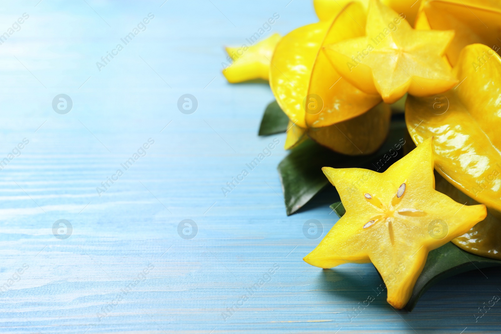 Photo of Delicious carambola fruits on light blue wooden table. Space for text