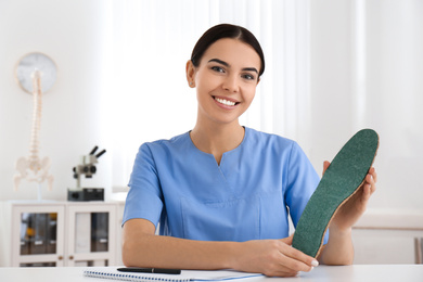 Photo of Young female orthopedist showing insole in clinic