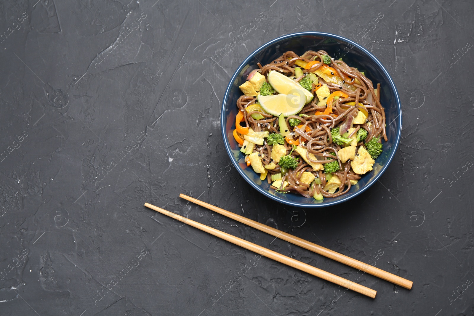 Photo of Stir-fry. Delicious cooked noodles with chicken and vegetables in bowl served on gray textured table, flat lay. Space for text