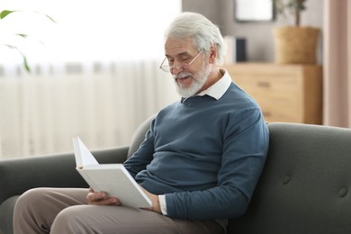 Portrait of happy grandpa reading book on sofa indoors