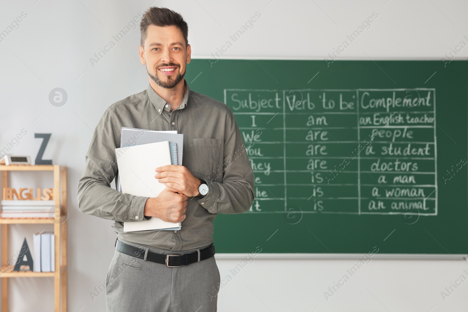 Photo of Happy teacher with stationery in classroom during English lesson