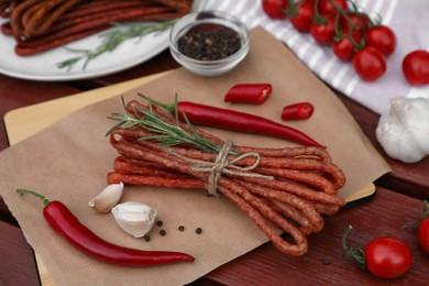 Photo of Bundles of delicious kabanosy with rosemary, peppercorn, garlic and chilli on wooden table