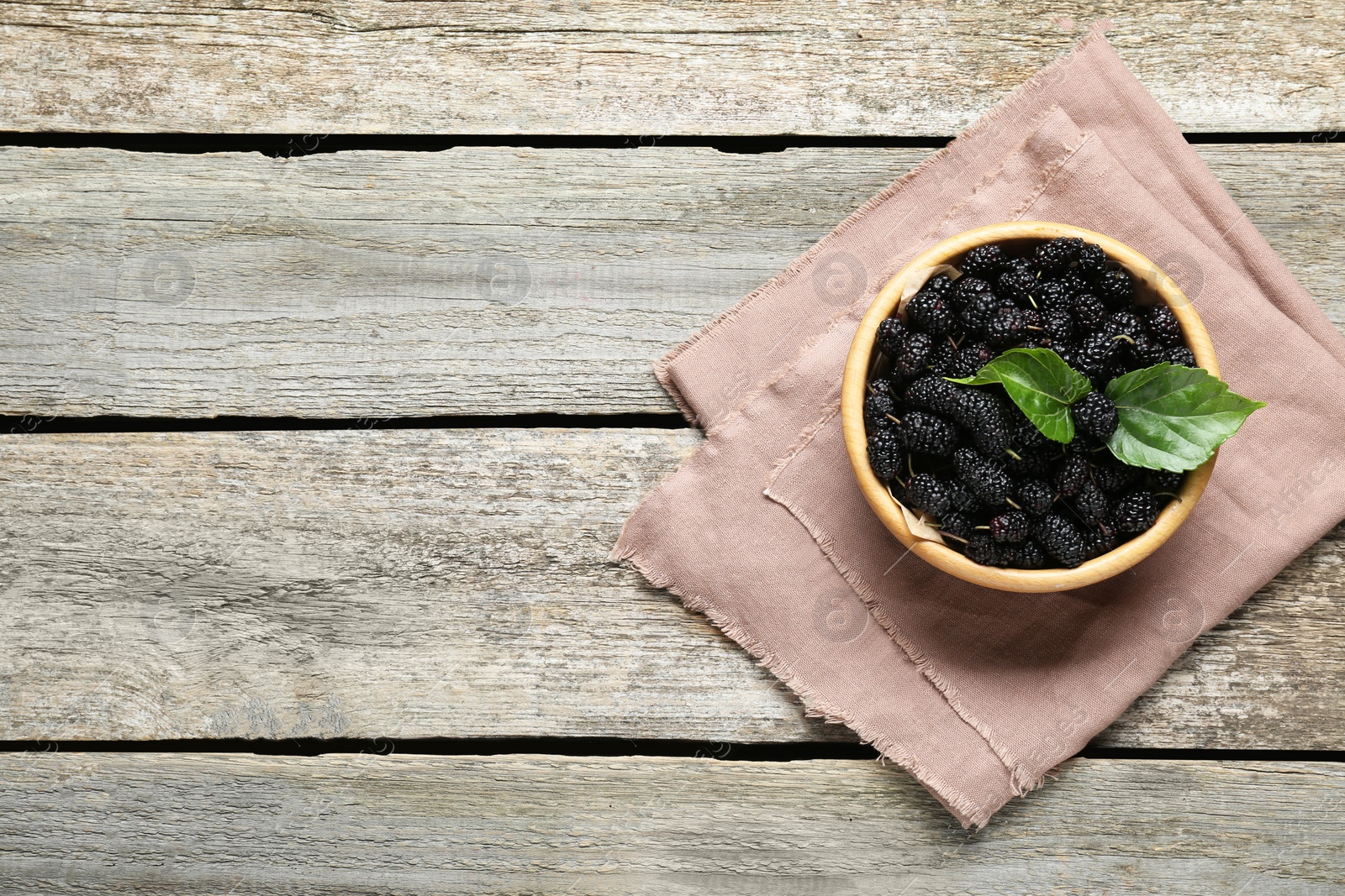 Photo of Bowl of delicious ripe black mulberries on wooden table, top view. Space for text