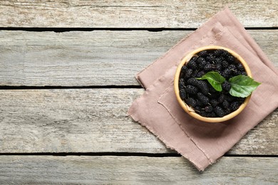 Bowl of delicious ripe black mulberries on wooden table, top view. Space for text