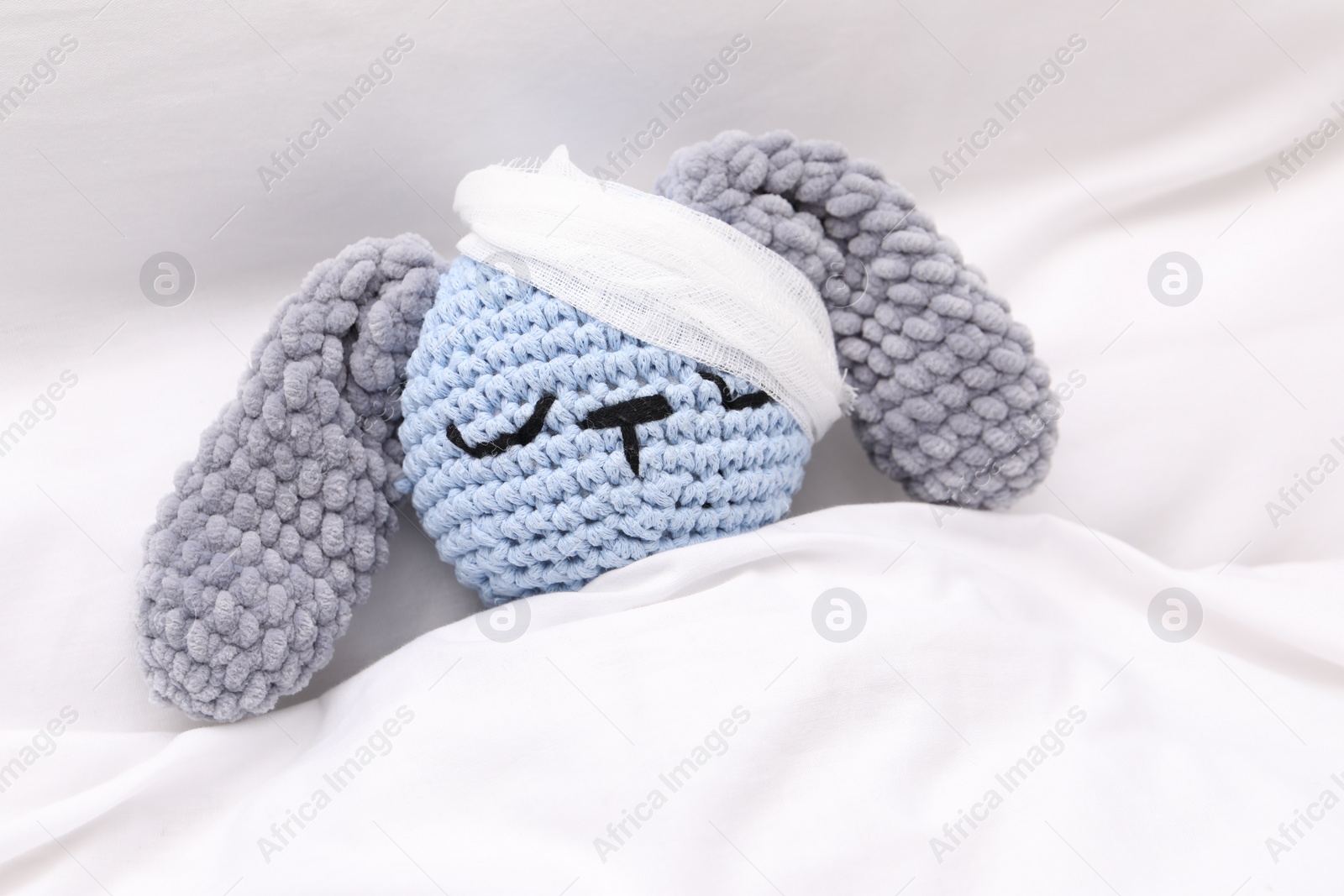 Photo of Toy cute bunny with bandage under blanket in bed