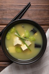 Photo of Bowl of delicious miso soup with tofu served on wooden table, top view