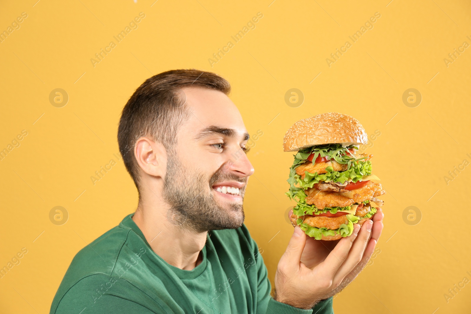 Photo of Young hungry man eating huge burger on color background