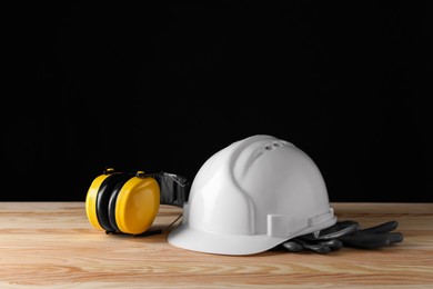 Hard hat, earmuffs and gloves on wooden table, space for text. Safety equipment