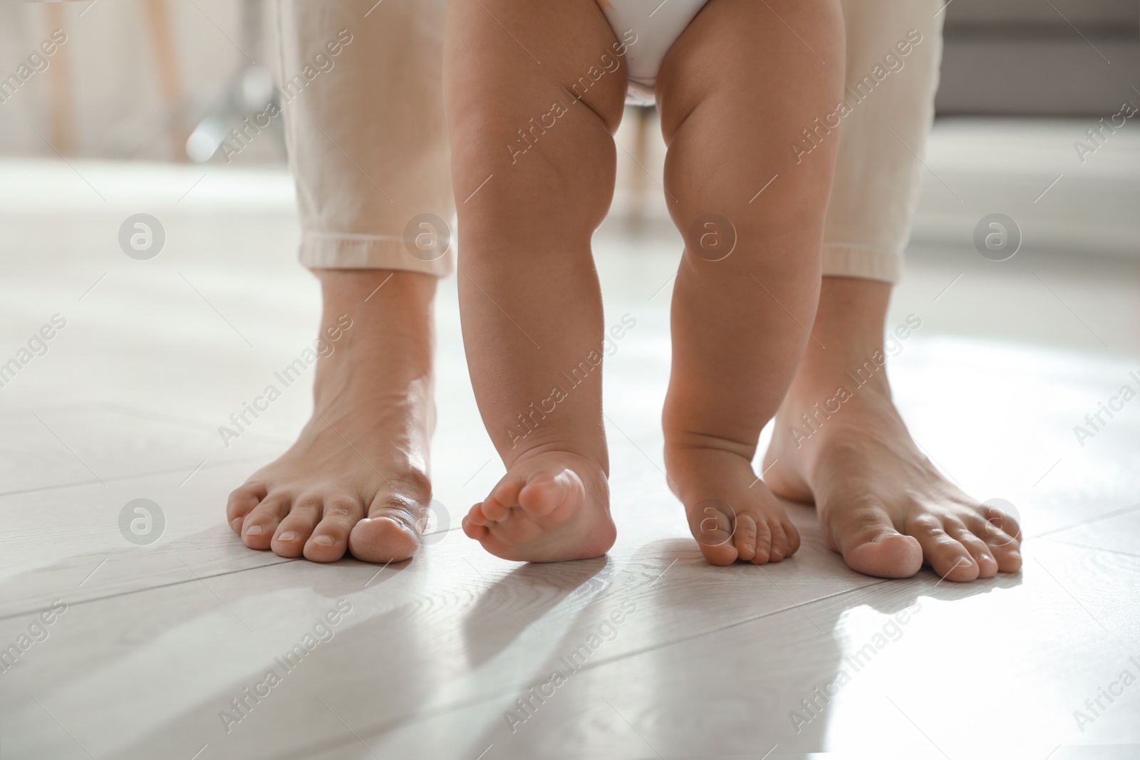 Photo of Mother supporting her baby daughter while she learning to walk at home, closeup