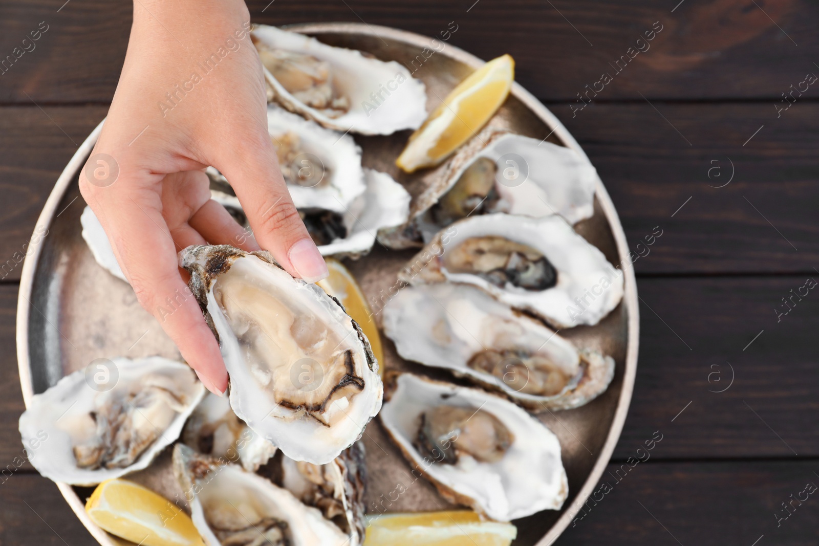 Photo of Top view of woman with fresh oyster over plate, focus on hand