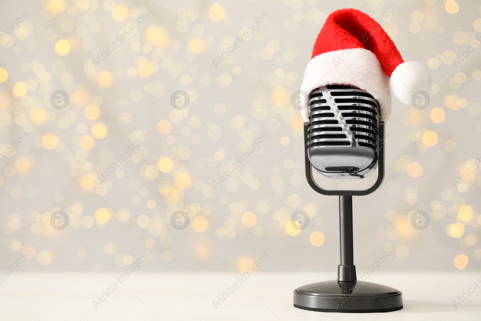 Photo of Retro microphone with Santa hat on table against blurred lights, space for text. Christmas music