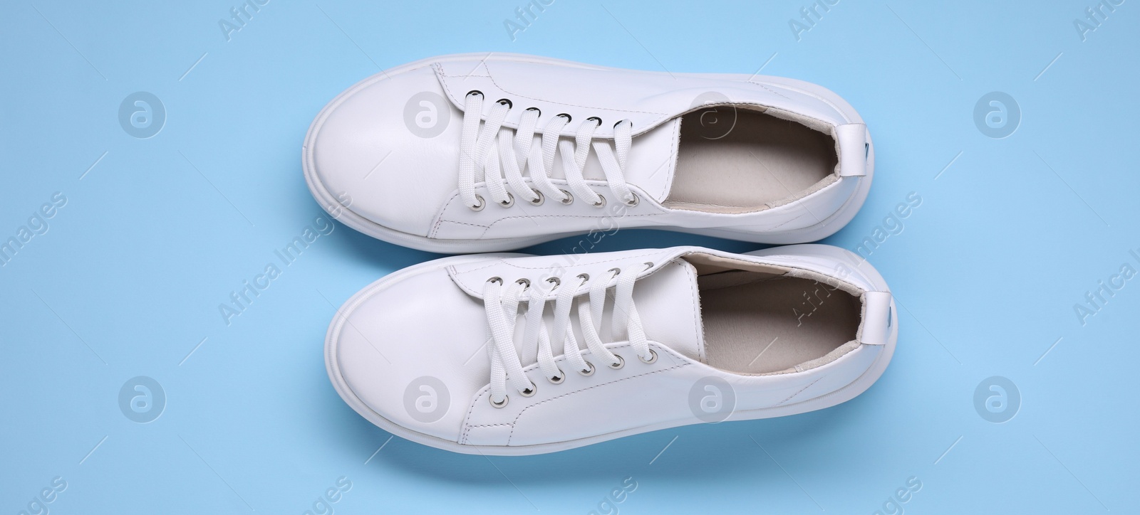 Photo of Pair of stylish white sneakers on light blue background, top view