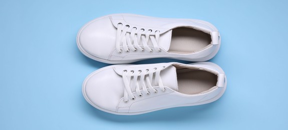 Photo of Pair of stylish white sneakers on light blue background, top view