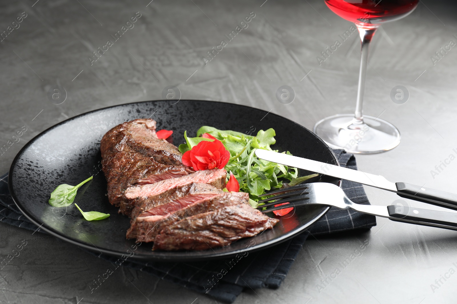 Photo of Delicious grilled beef meat served with greens on grey table