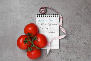 Photo of Notebook with calculated glycemic load for tomatoes, measuring tape and fresh vegetables on grey table, flat lay