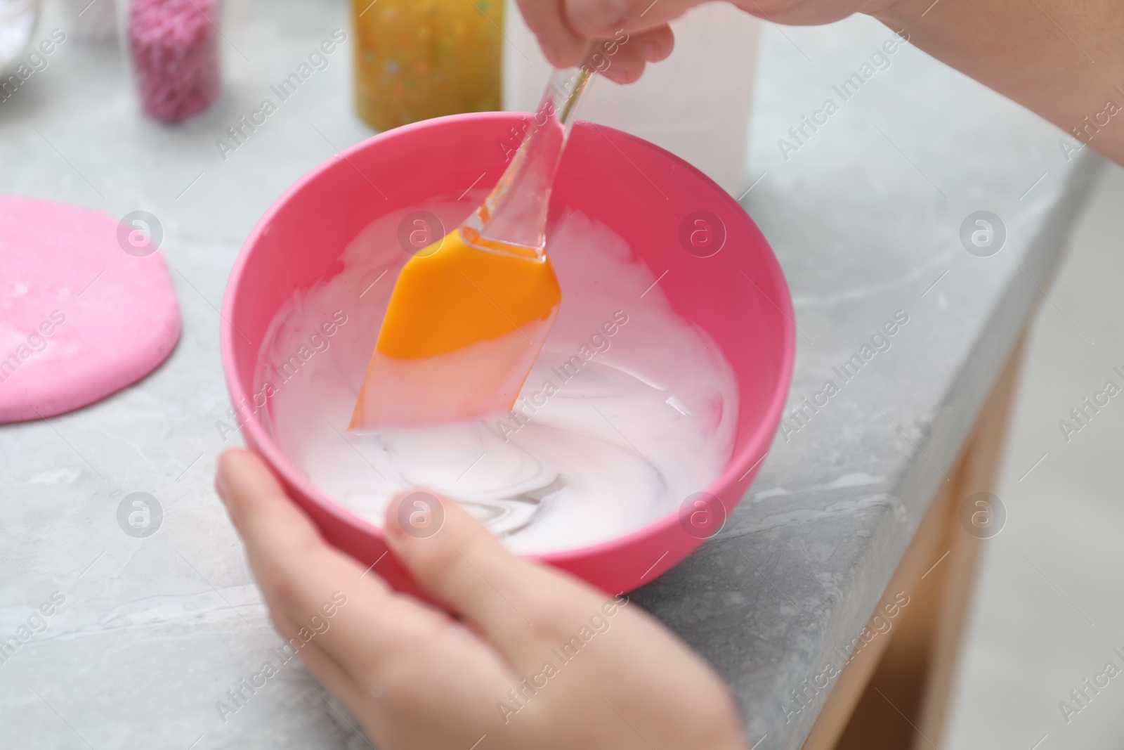 Photo of Little girl mixing ingredients with silicone spatula at table, closeup. DIY slime toy