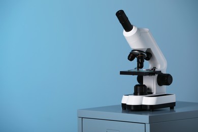 Photo of Modern microscope on table against blue background. Space for text