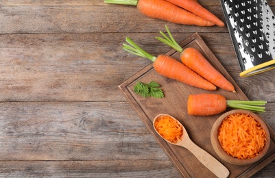 Photo of Board with fresh and grated carrots on wooden table, flat lay. Space for text