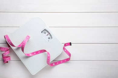 Bathroom scale, measuring tape and space for text on white wooden floor, top view. Weight loss concept