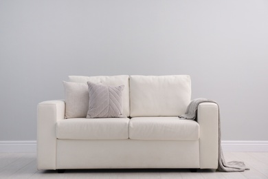 Photo of Comfortable white sofa near light wall indoors, space for text. Simple interior