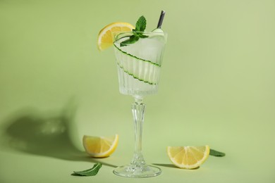 Photo of Glass of tasty fresh cucumber water with mint and sliced lemon on light green background