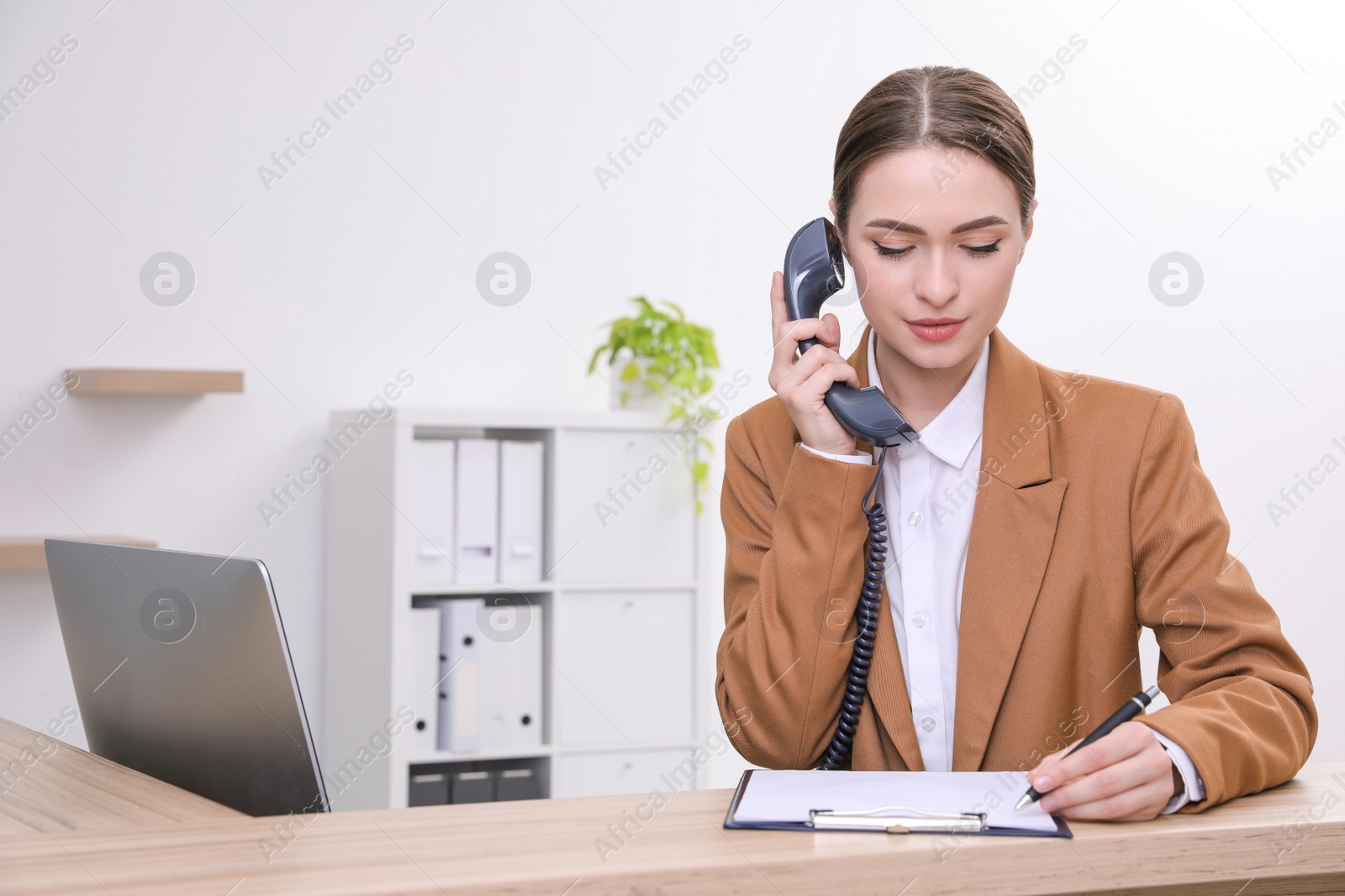 Photo of Female receptionist with clipboard talking on phone at workplace. Space for text