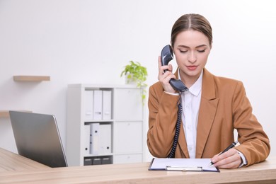 Female receptionist with clipboard talking on phone at workplace. Space for text