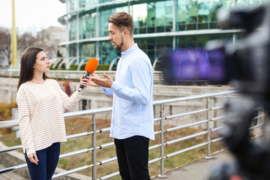 Photo of Young journalist interviewing man on city street
