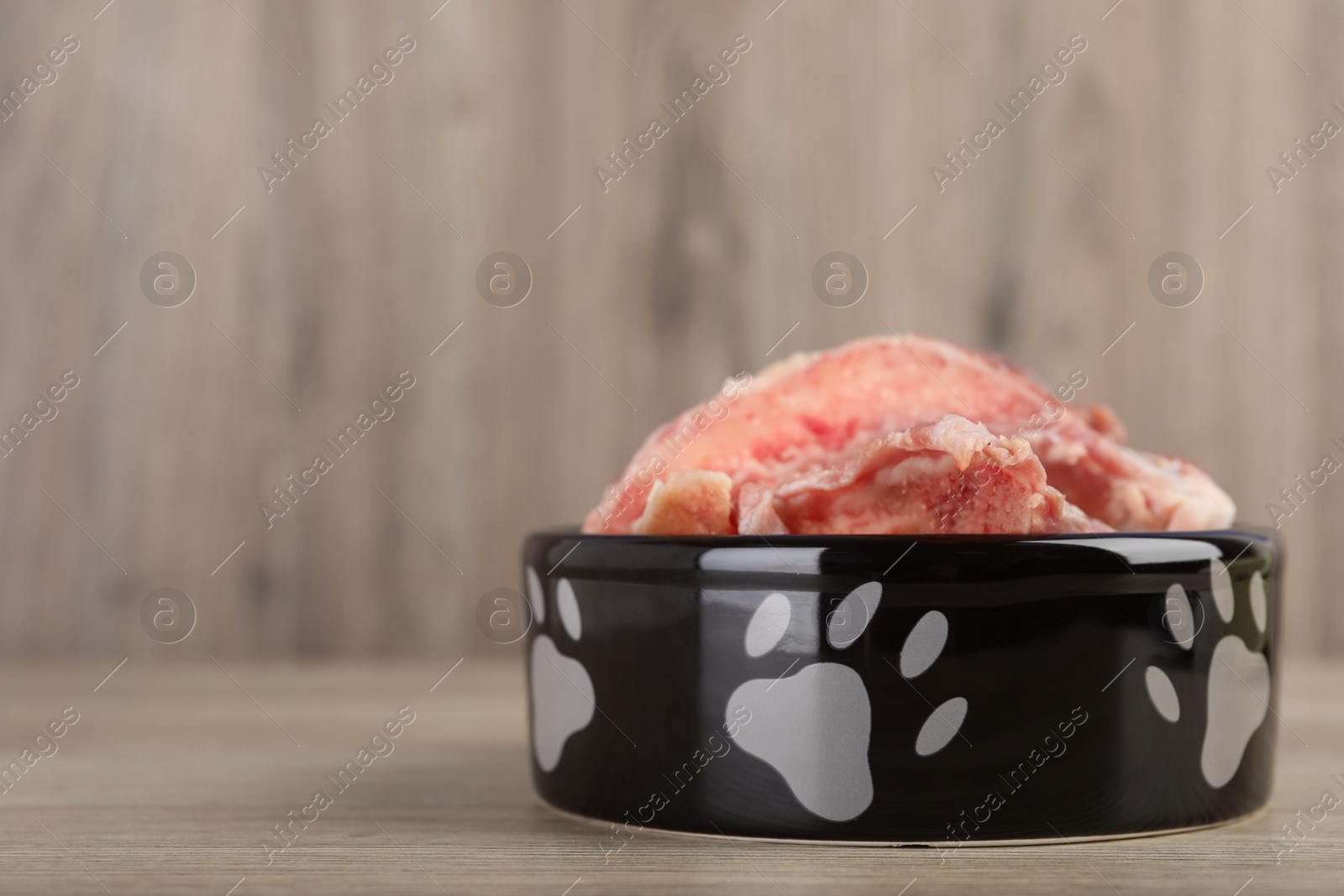 Photo of Feeding bowl with raw meaty bones on wooden table. Space for text