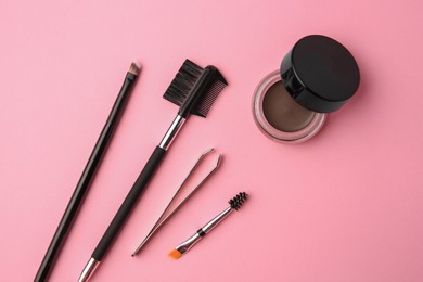 Eyebrow pomade with henna effect and professional tools on pink background, flat lay