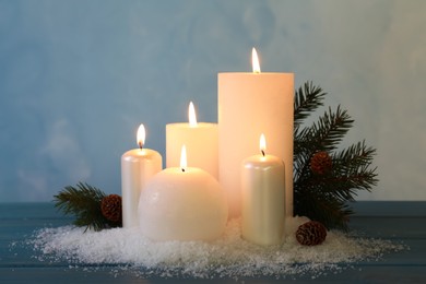 Photo of Burning candles with fir tree branch, cones and artificial snow on blue wooden table. Christmas atmosphere