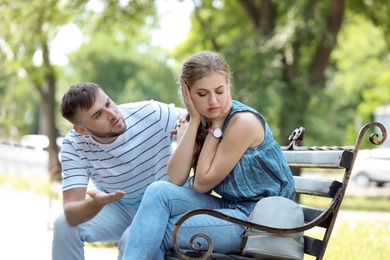 Photo of Young couple arguing while sitting on bench in park. Problems in relationship