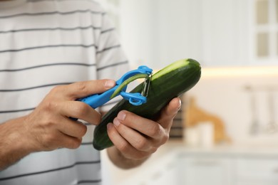 Photo of Man peeling cucumber in kitchen, closeup. Preparing vegetable