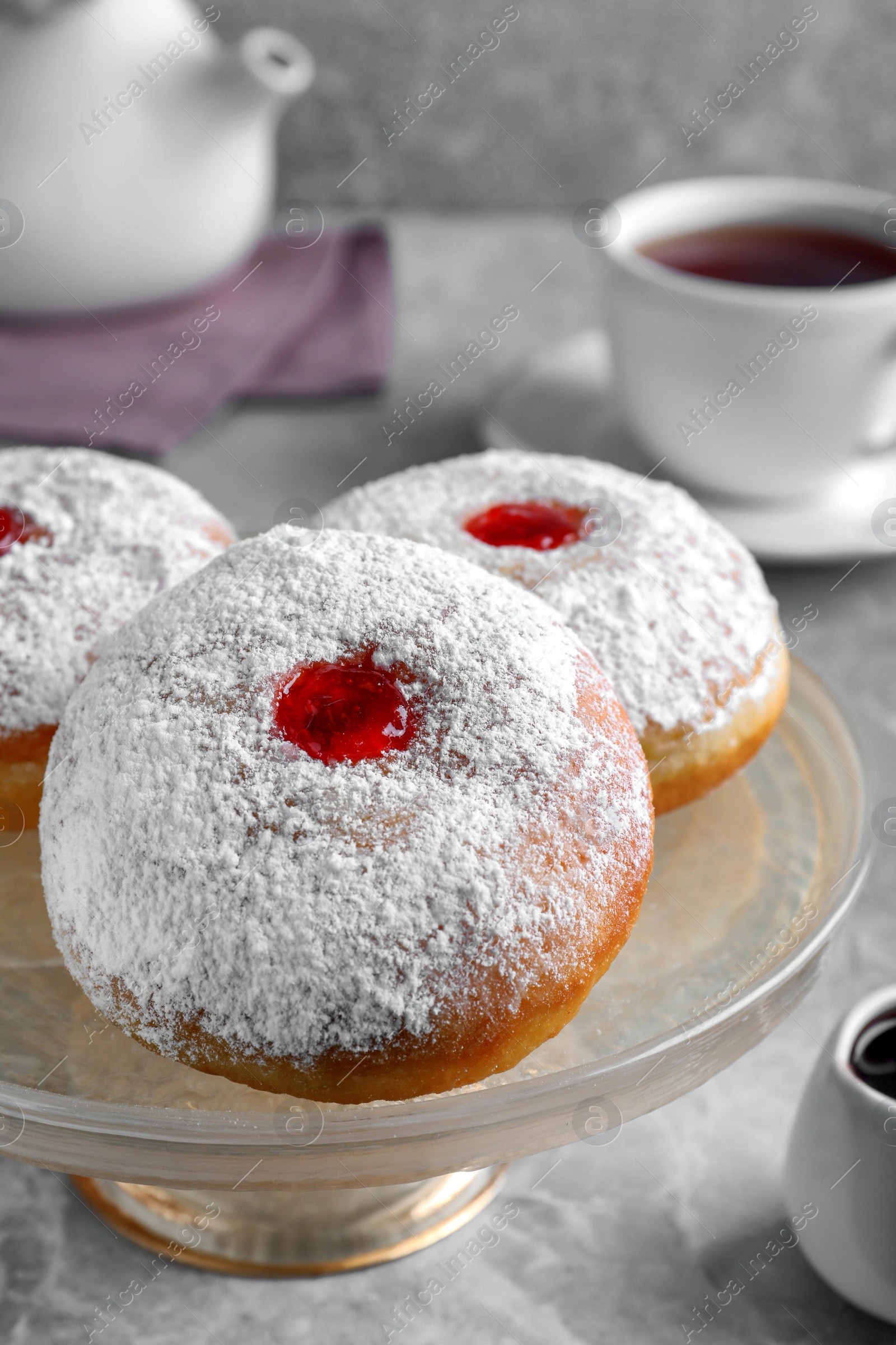 Photo of Pastry stand with delicious jelly donuts on grey table, closeup