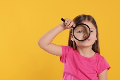 Cute little girl looking through magnifier on yellow background. Space for text