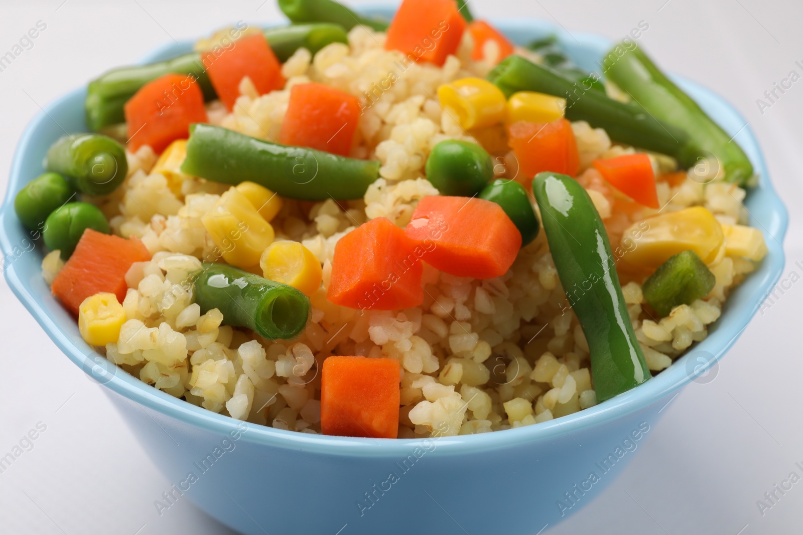 Photo of Delicious bulgur with vegetables in bowl on white table, closeup