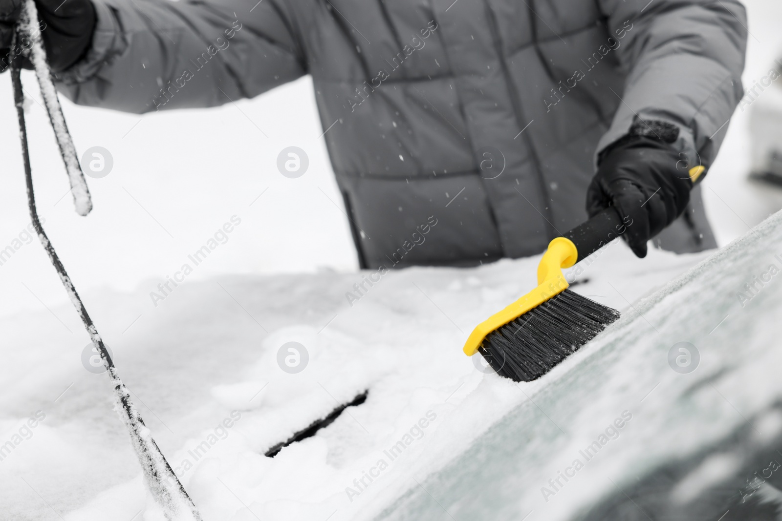 Photo of Man cleaning snow from car windshield outdoors, closeup