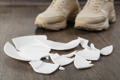 Photo of Woman in sneakers standing near broken plate on floor, closeup