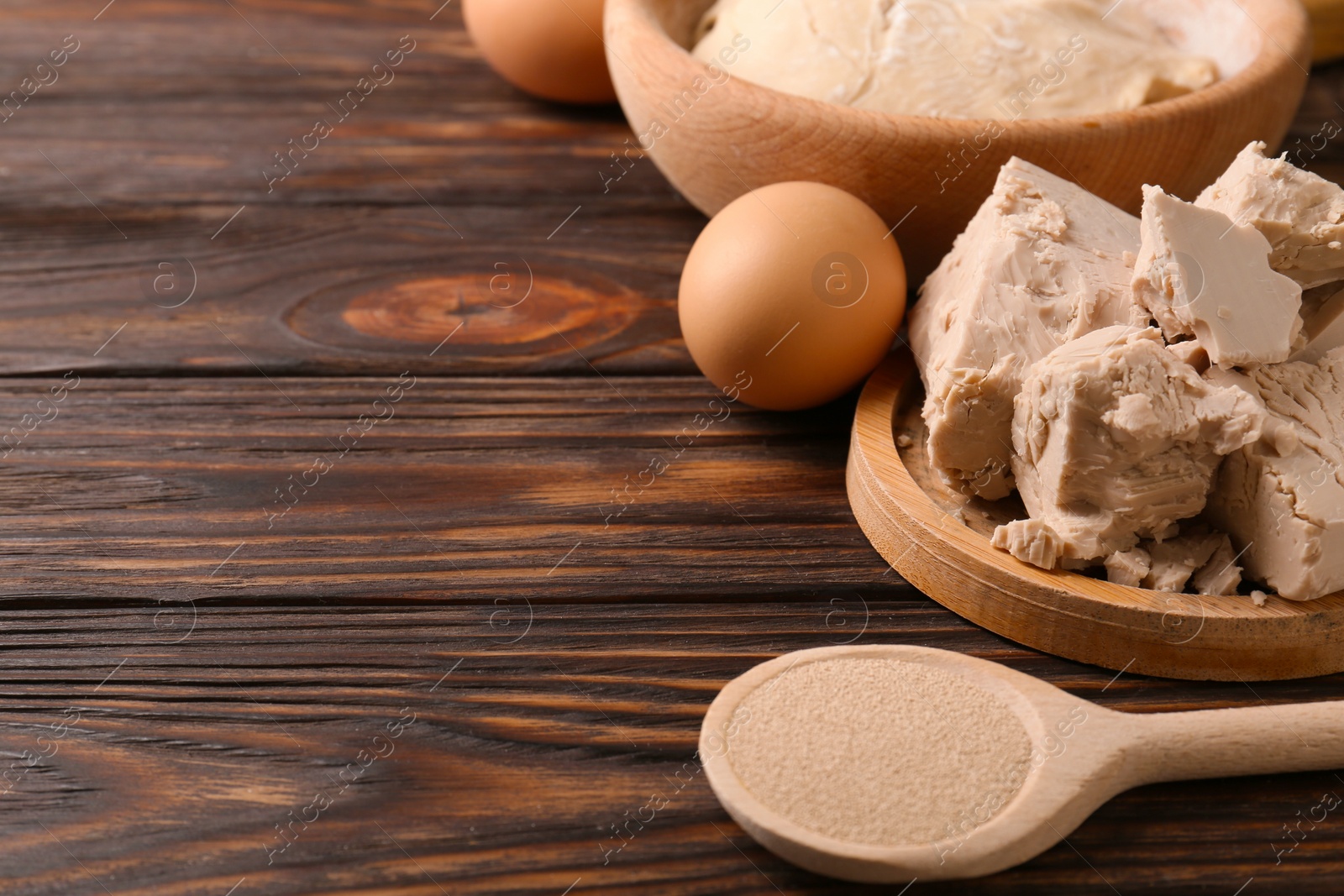 Photo of Compressed and dry granulated yeast, eggs and dough on wooden table, space for text
