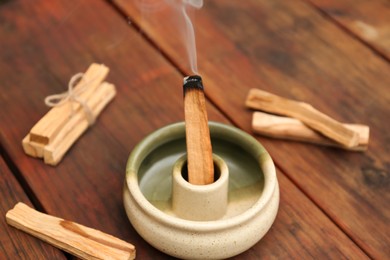 Photo of Palo Santo stick smoldering in holder on wooden table